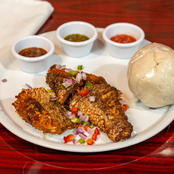 Fried fish with chopped vegetables, three dipping sauces, and fufu on a white plate.