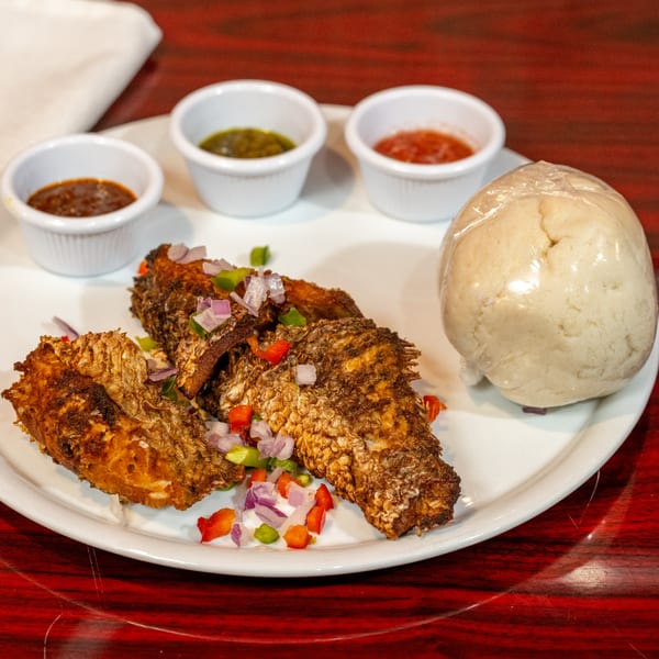 African fried fish with chopped vegetables, three dipping sauces, and a wrapped fufu ball.