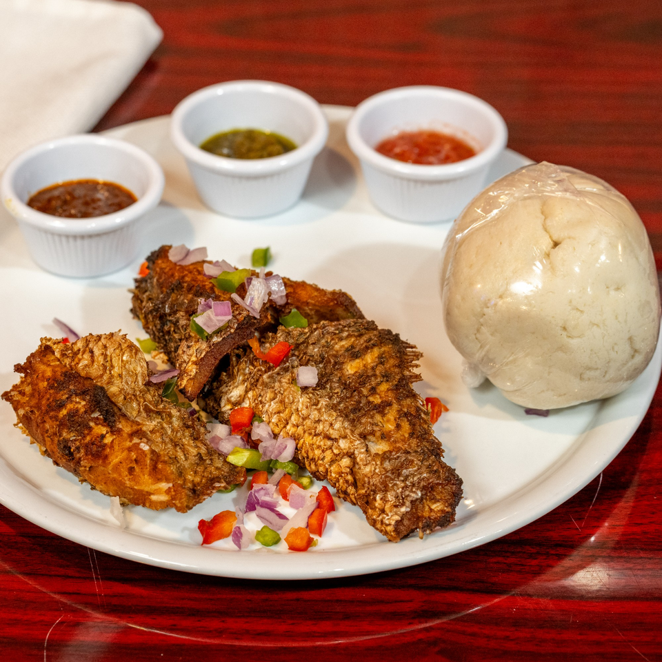 African fried fish with chopped vegetables, three dipping sauces, and a wrapped fufu ball.