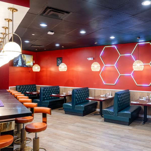 El Afrik Cuisine and Bar interior with red walls, teal booths, orange bar stools, and hexagon neon lights.