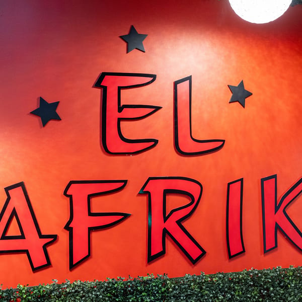Red El Afrik Cuisine and Bar sign with black stars and green foliage below.