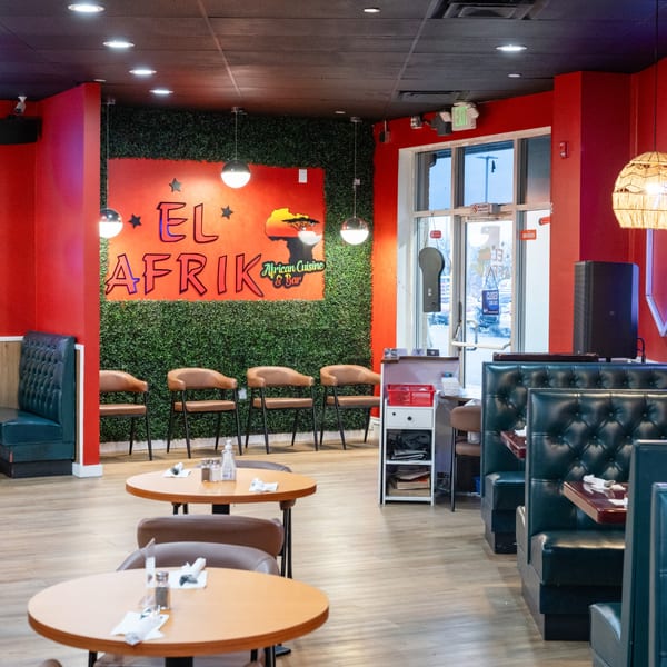 Interior of El Afrik Cuisine and Bar with red walls, green faux-foliage, and seating.