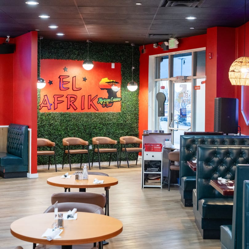 Interior of El Afrik Cuisine and Bar with red walls, green faux-foliage, and seating.