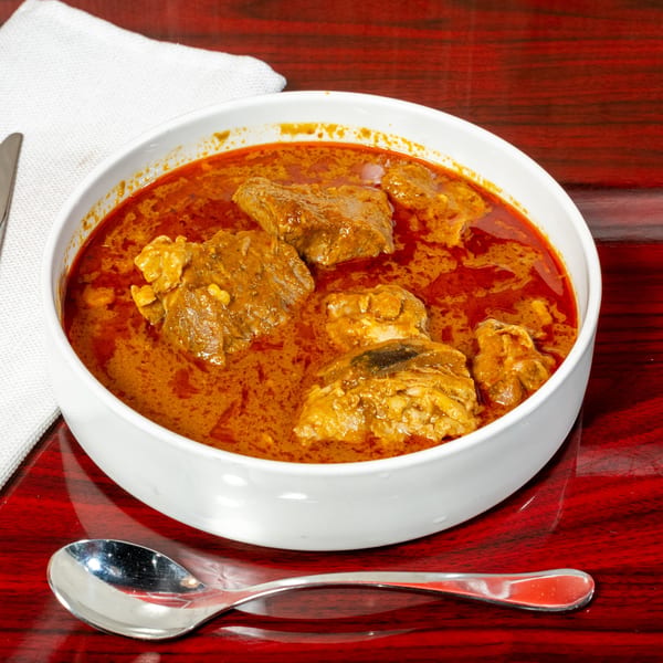 A white bowl of El Afrik Cuisine and Bar's African stew with meat in a rich red sauce.