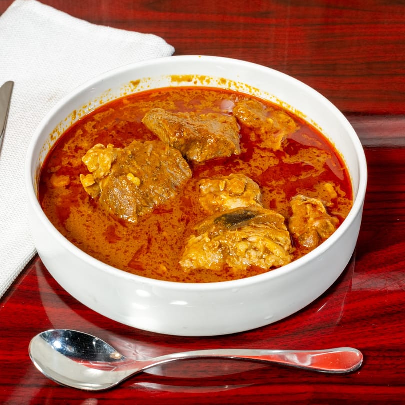 A white bowl of El Afrik Cuisine and Bar's African stew with meat in a rich red sauce.