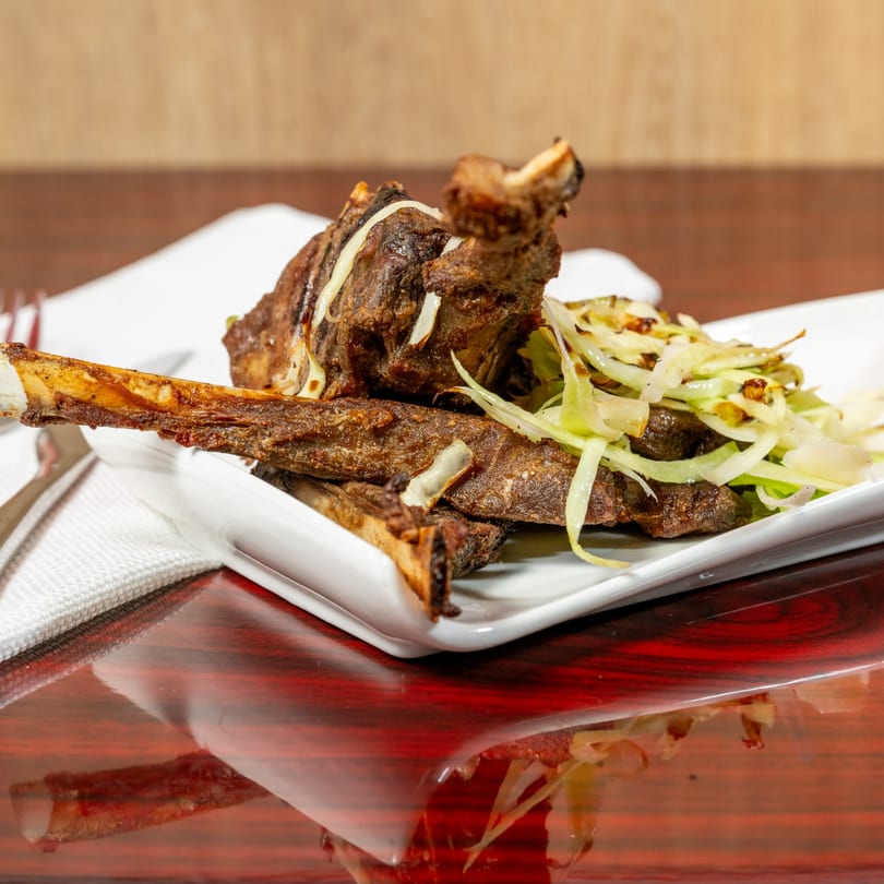 El Afrik Cuisine and Bar's African-style grilled ribs with shredded cabbage on a white plate.