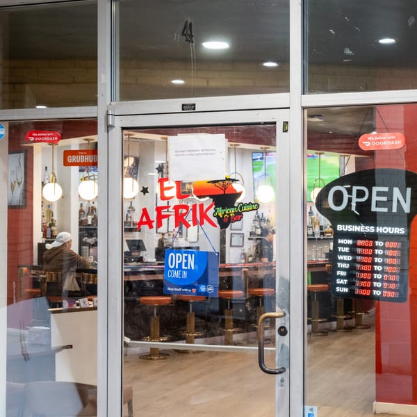 The glass entrance of El Afrik Cuisine and Bar, showing the interior bar area and business hours.