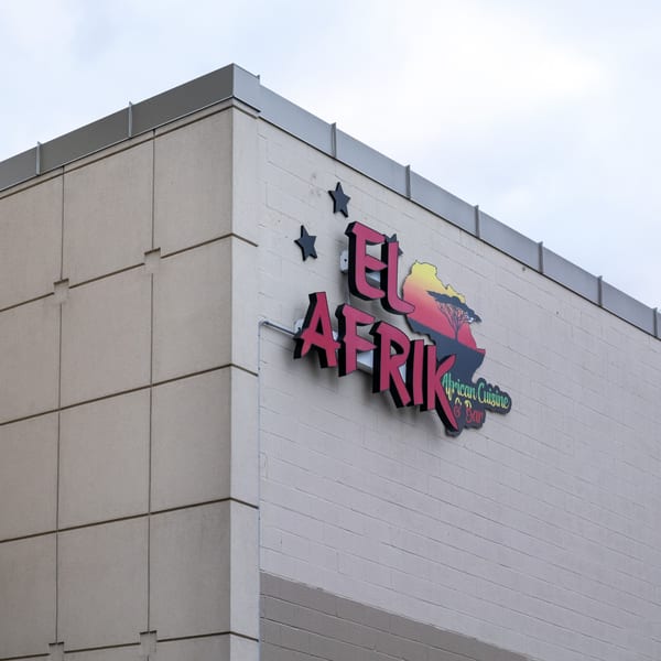 El Afrik Cuisine and Bar sign on a building, featuring a map of Africa with a sunset and acacia tree.