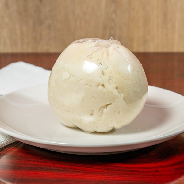 A round, light-colored African fufu, wrapped in plastic, sits on a white plate.