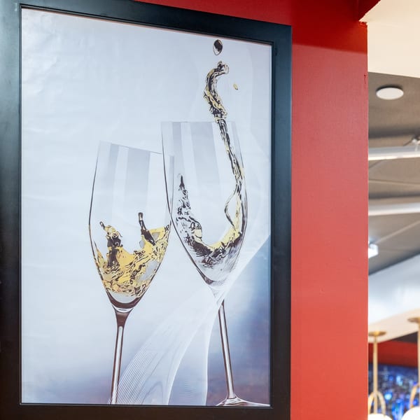 Framed artwork of two wine glasses with liquid splashing, hanging on a red wall.