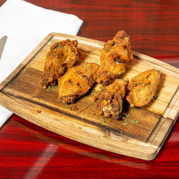 Crispy fried chicken wings, garnished with herbs, served on a wooden board at El Afrik Cuisine.