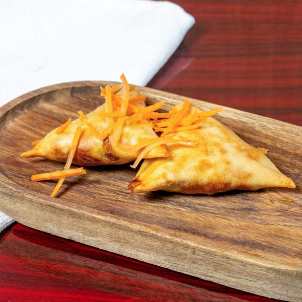 Two golden-brown African samosas topped with shredded carrots on a wooden serving tray.