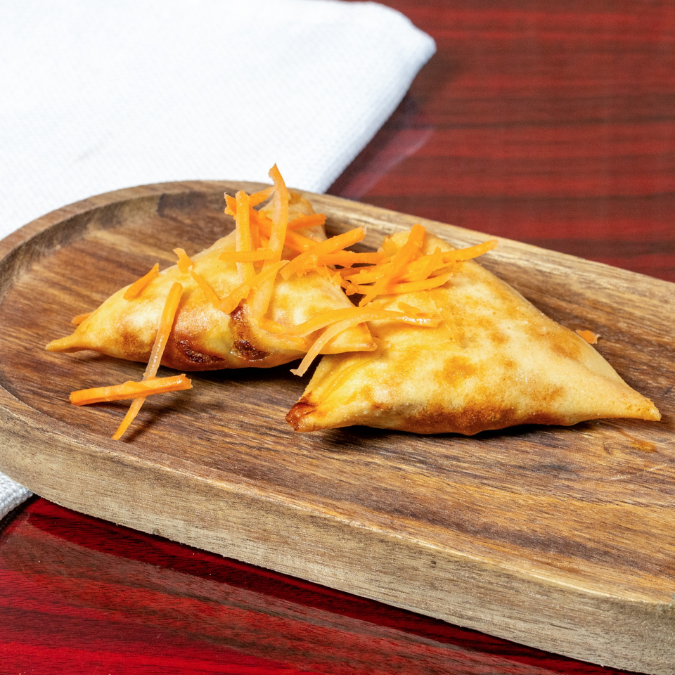 Two golden-brown African samosas topped with shredded carrots on a wooden serving tray.